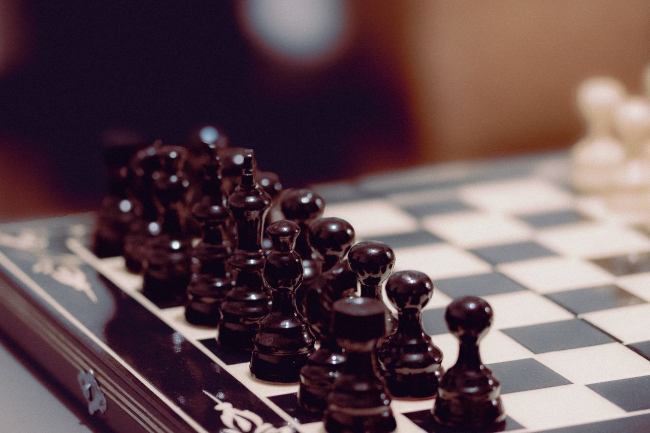 Close-up of black chess pieces aligned on a chessboard, ready for play.