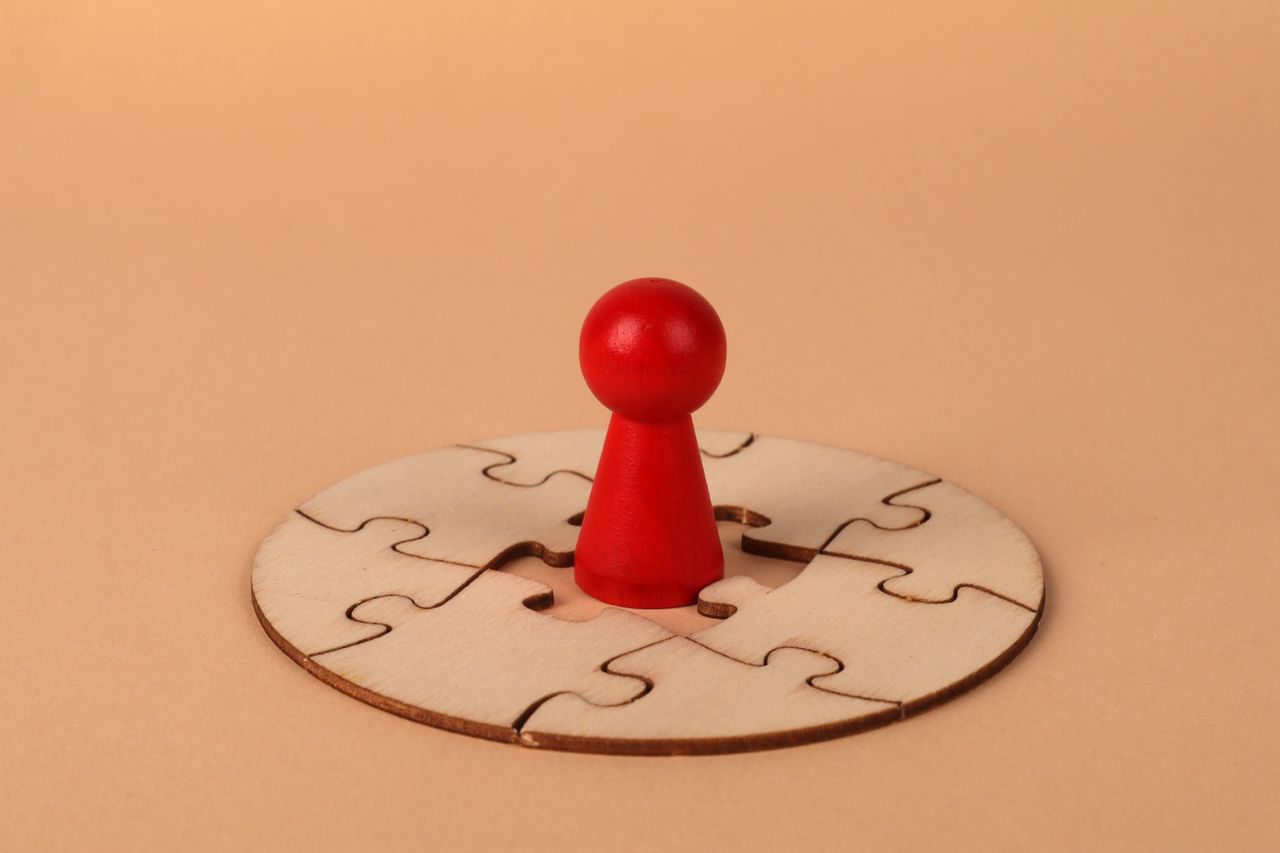 A red pawn stands on a wooden circular puzzle, symbolizing strategy and problem-solving.